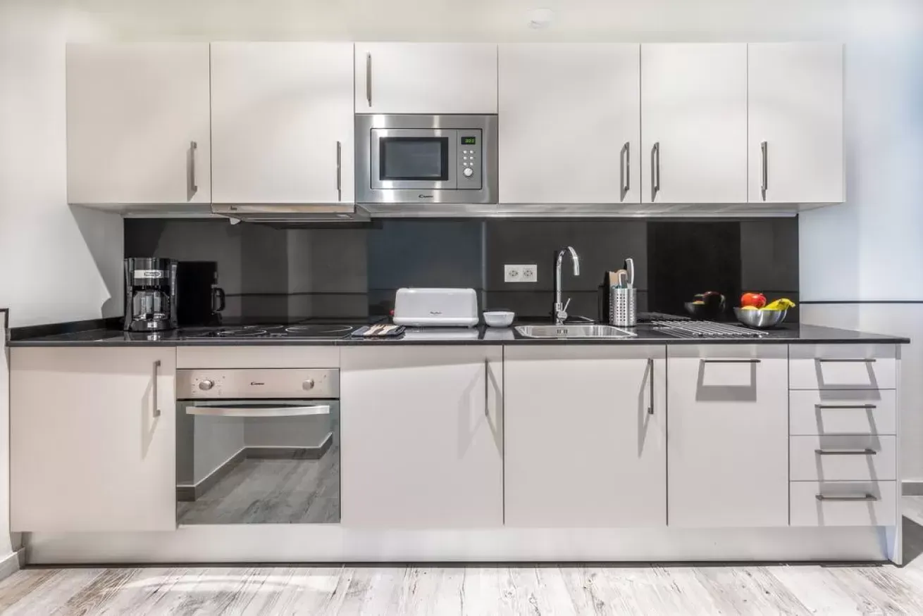 Cocina moderna blanca con salpicadero negro, electrodomésticos de acero inoxidable y cafetera de encimera.