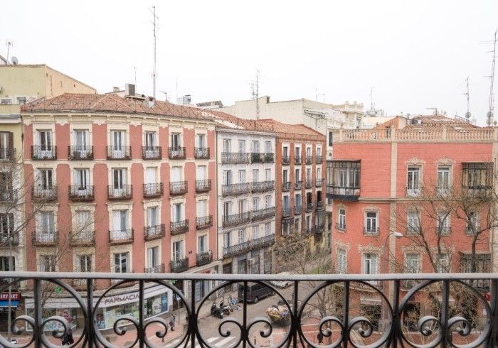 Vista desde un balcón de edificios de apartamentos de colores pastel y una calle arbolada de la ciudad.