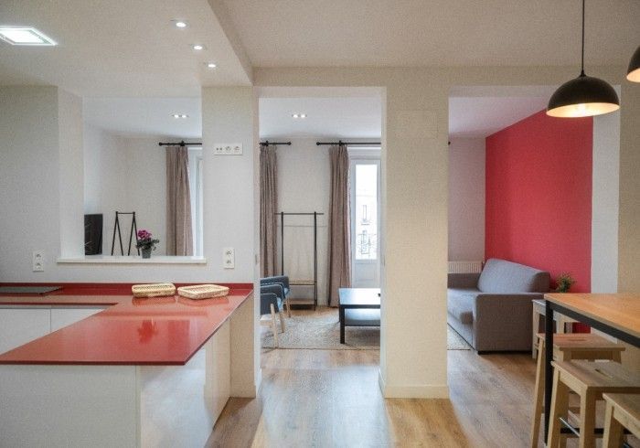 Interior de apartamento moderno con cocina abierta, isla de coral y una acogedora sala de estar con pared decorativa rosa.