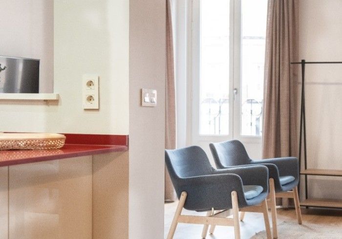 Moderna sala de espera con sillas azules, un mostrador rojo y una ventana con cortinas.