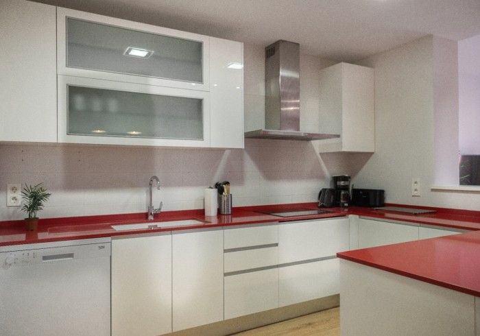 Cocina moderna blanca con encimeras, armarios, fregadero y electrodomésticos de acero inoxidable en color rojo.