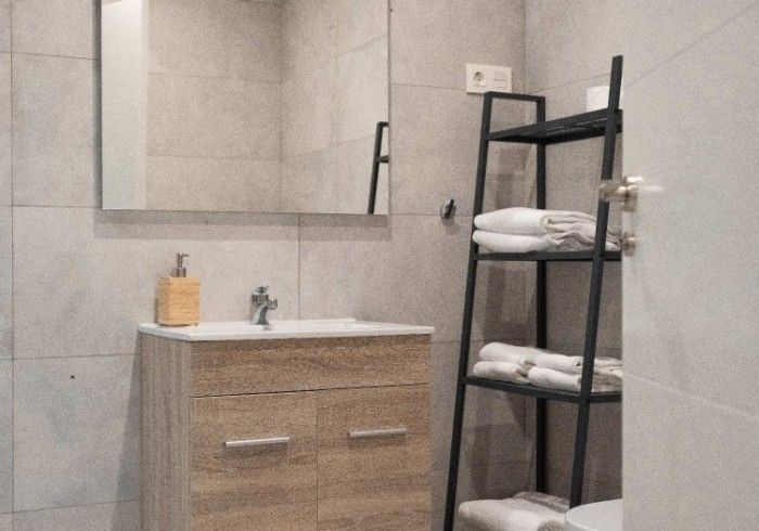 Baño moderno con espejo, tocador de madera, lavabo y estantes negros con toallas dobladas.