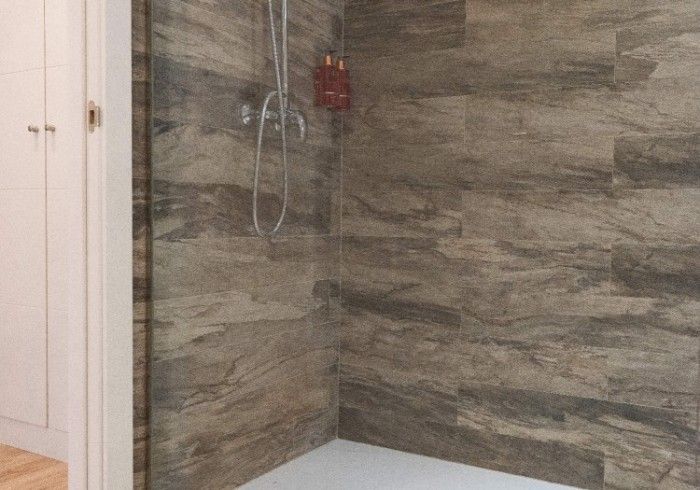 Ducha moderna con azulejos, paredes de piedra gris y un mueble blanco al lado.