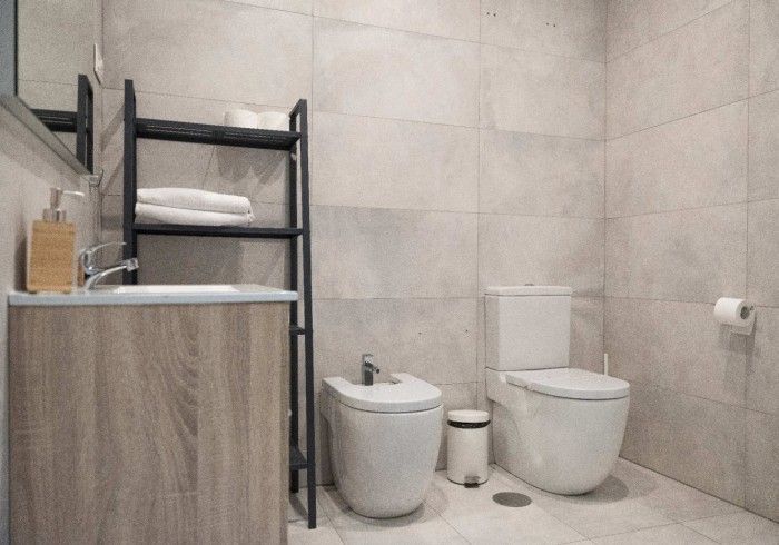 Baño moderno con inodoro, bidé, lavabo y estantería negra contra paredes alicatadas.