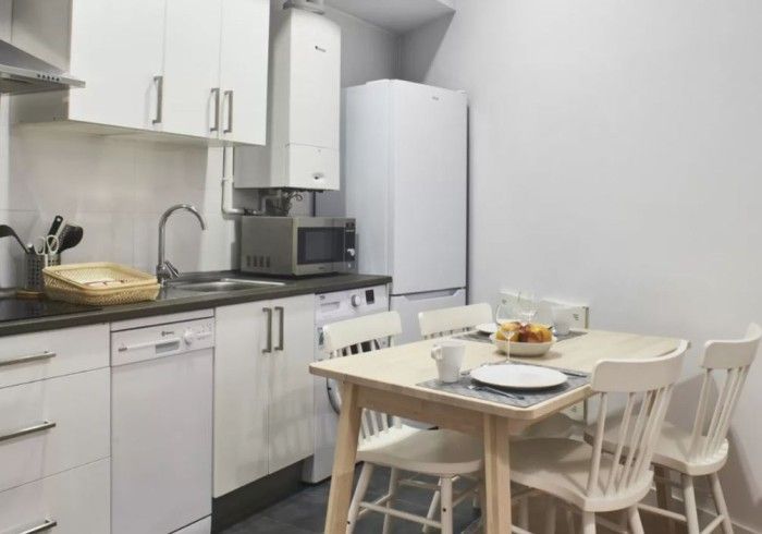 Pequeña cocina blanca con mesa de comedor para dos personas y microondas en la encimera.