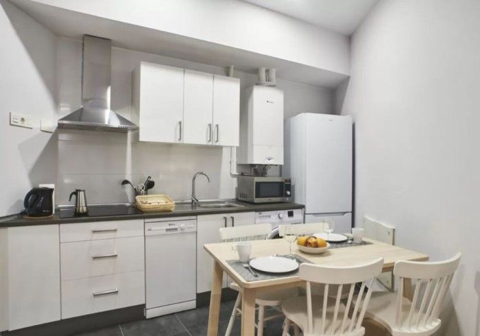 Cocina moderna blanca con mesa de comedor, armarios, estufa, fregadero y pequeños electrodomésticos.