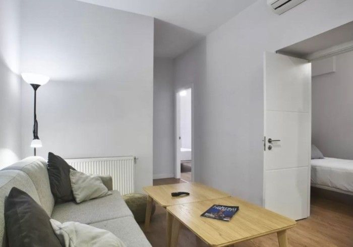 Sala de estar moderna con paredes blancas, sofá gris, mesa de centro de madera y lámpara de pie cerca de un pasillo.