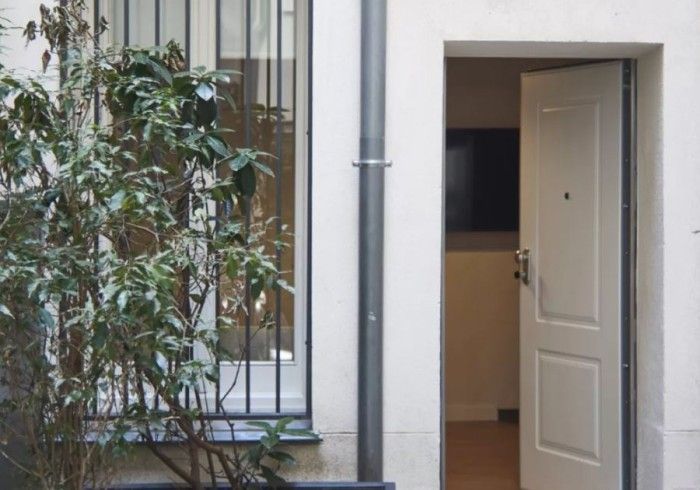 Entrada abierta en un patio junto a una ventana enrejada y un árbol en maceta.