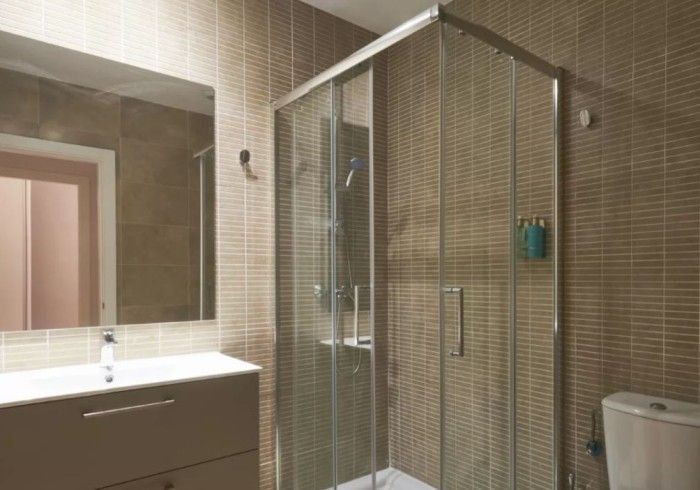 Baño moderno con espejo grande, lavabo, cabina de ducha alicatada e inodoro.