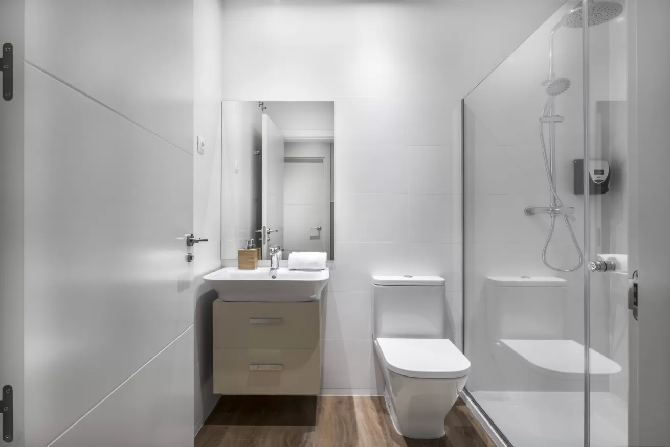 Baño moderno con ducha de cristal, inodoro, lavabo con mueble y suelo de madera.