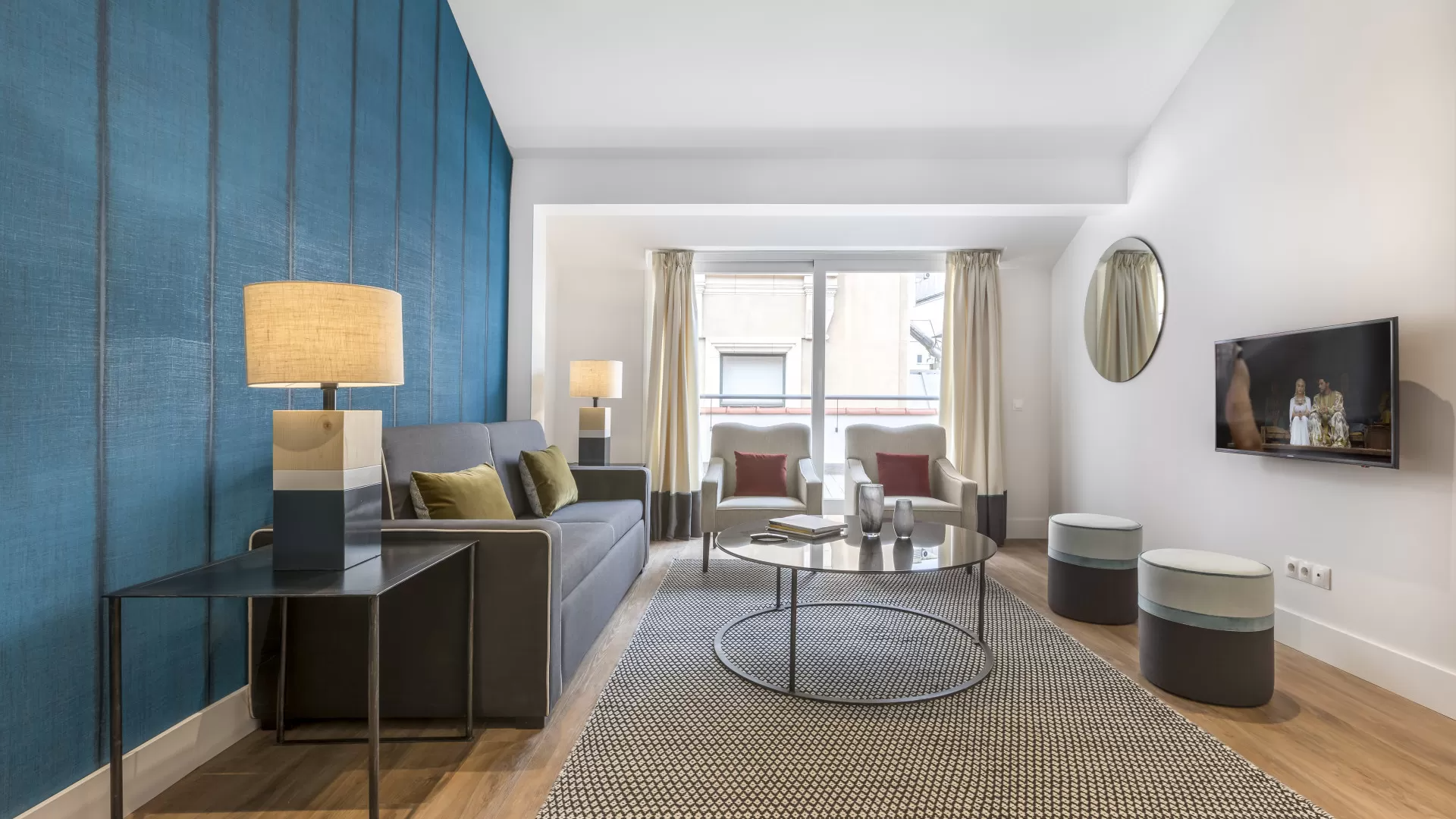 Sala de estar moderna con pared decorativa azul, sofá gris, alfombra estampada y televisor montado en la pared.