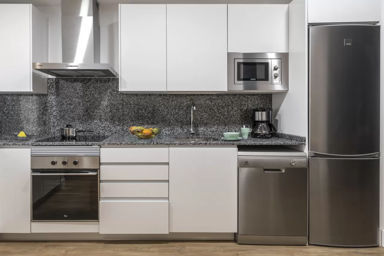 Cocina moderna con electrodomésticos de acero inoxidable, gabinetes blancos y protector contra salpicaduras de granito.