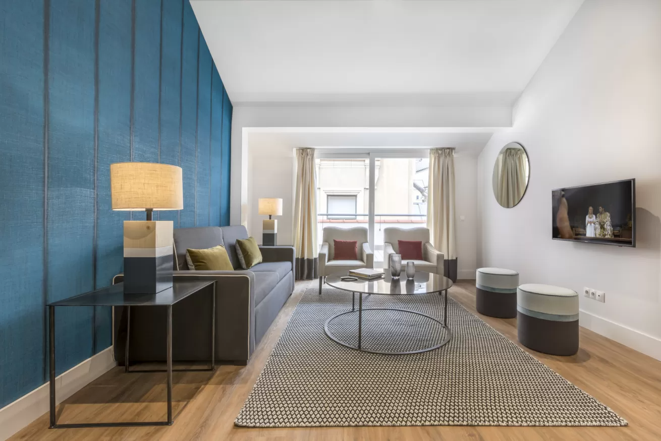 Sala de estar moderna con pared decorativa azul, sofá gris, alfombra estampada y ventanas luminosas.