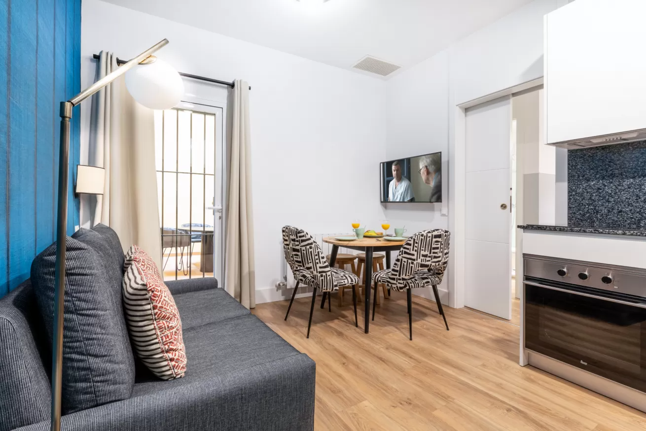 Comedor y sala de estar compactos con sofá, mesa de cristal y cocina americana en un luminoso apartamento.