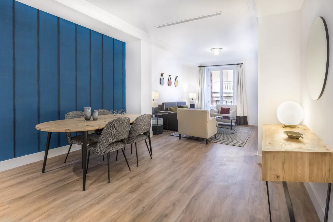 Salón-comedor moderno con pared decorativa azul, suelos de madera clara y muebles en tonos neutros.