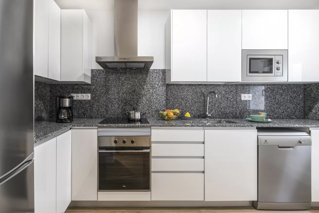 Cocina moderna blanca con electrodomésticos de acero inoxidable y salpicadero de azulejos de mosaico.