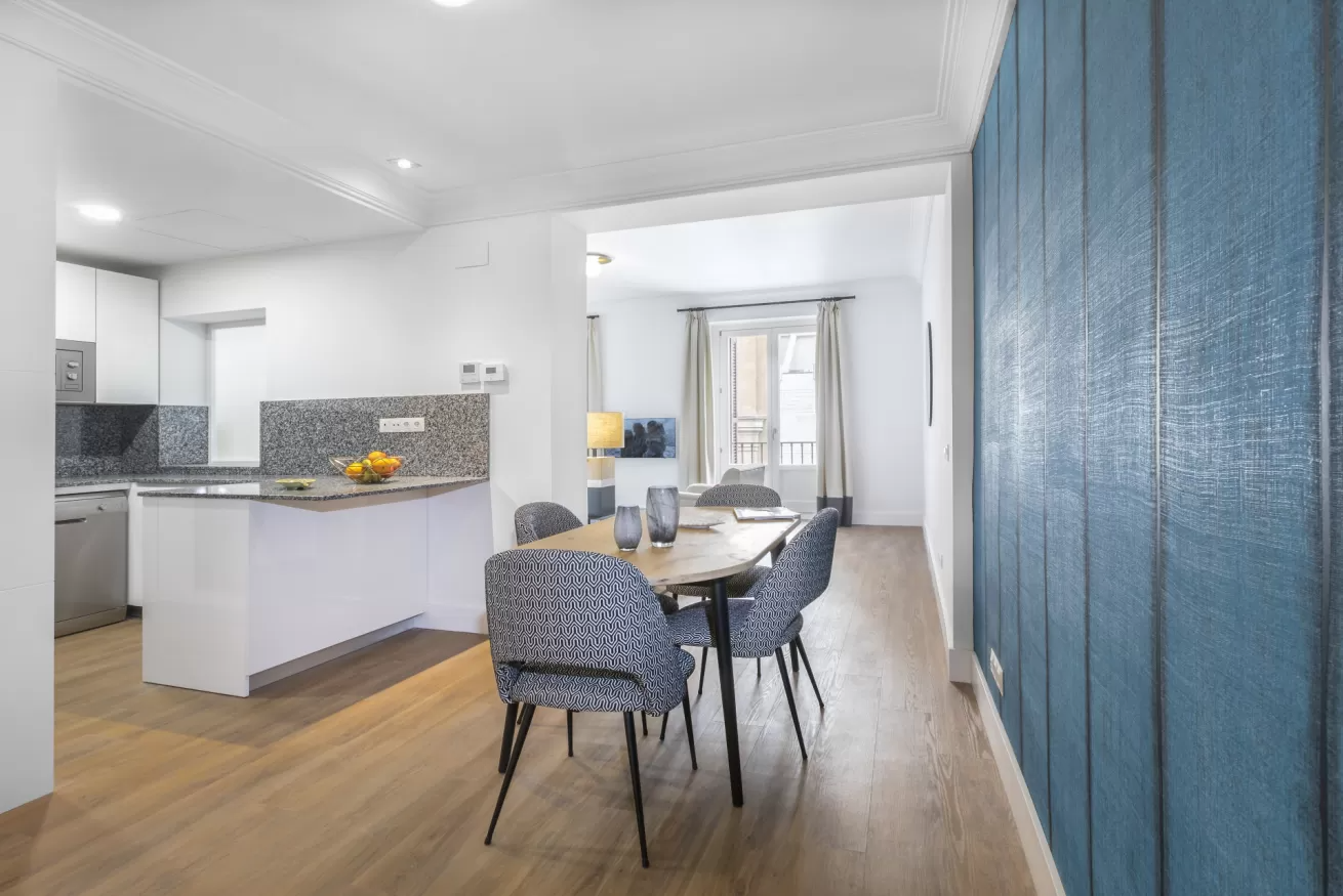 Zona de comedor y cocina moderna de planta abierta con armarios blancos, suelos de madera y paneles de pared.