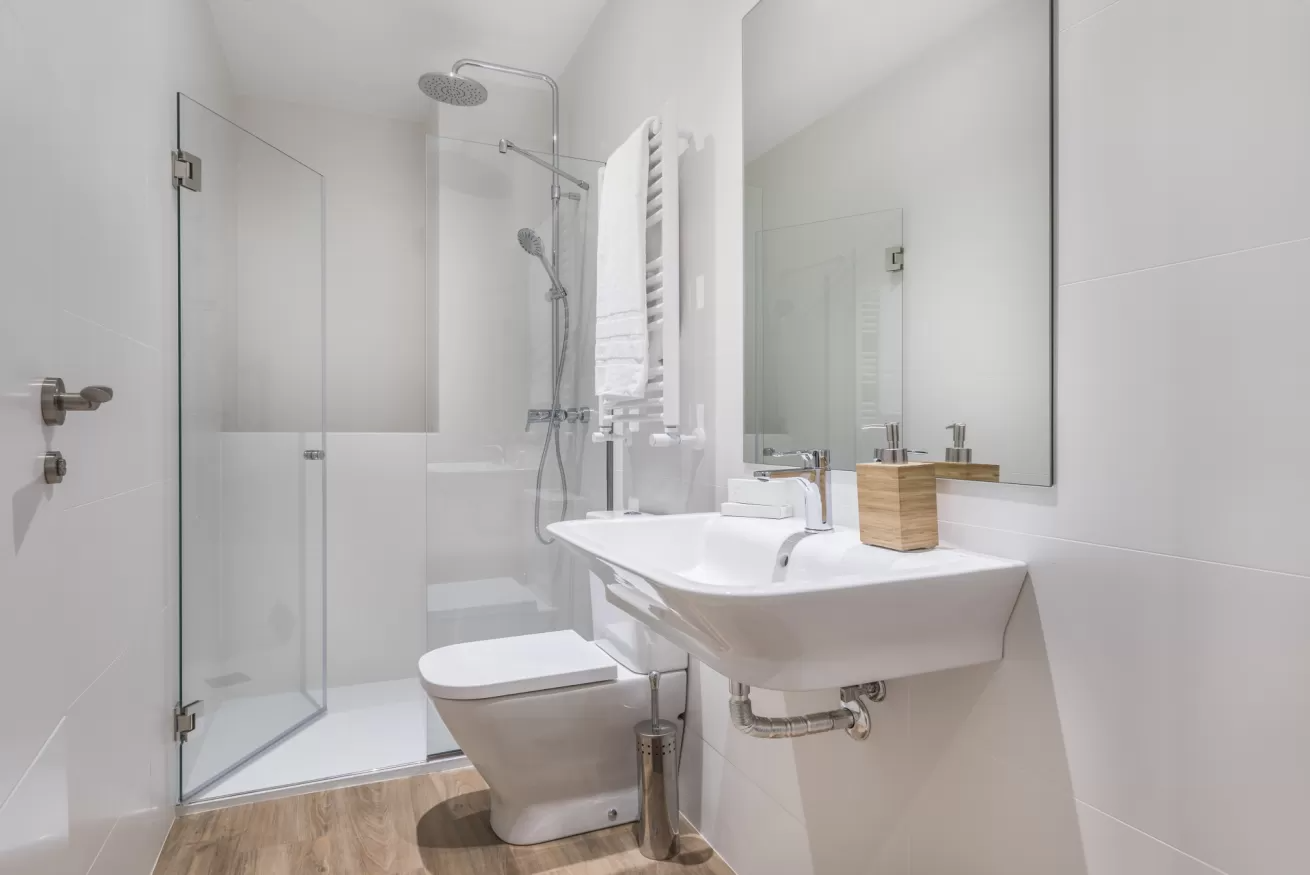 Baño moderno y luminoso con ducha de cristal, inodoro, lavabo y espejo grande.