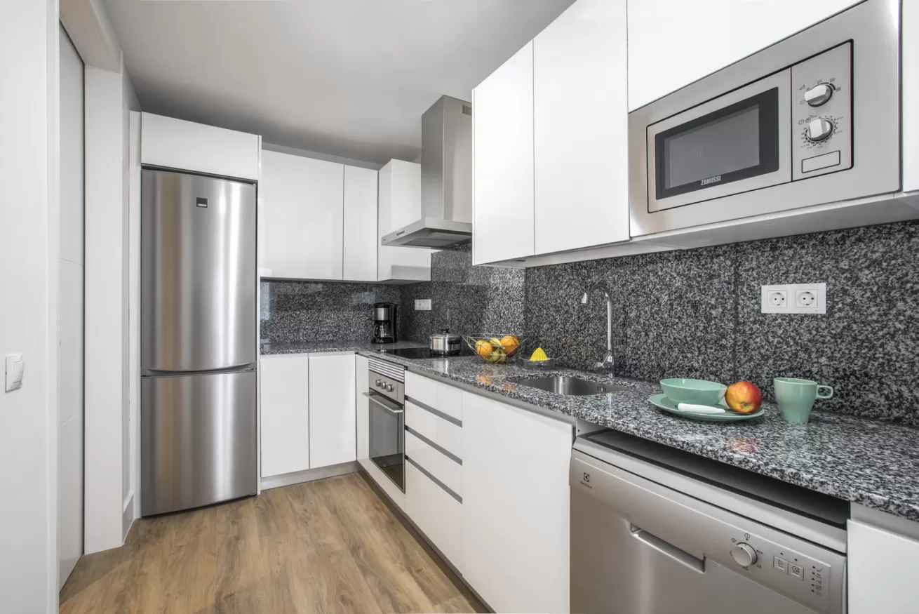 Cocina moderna blanca con electrodomésticos de acero inoxidable, salpicadero de azulejos grises y suelo de madera.