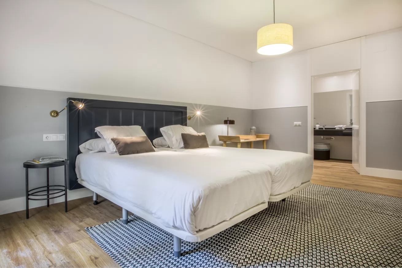 Dormitorio moderno con una cama grande, cabecero gris, alfombra estampada e iluminación tenue en la pared.