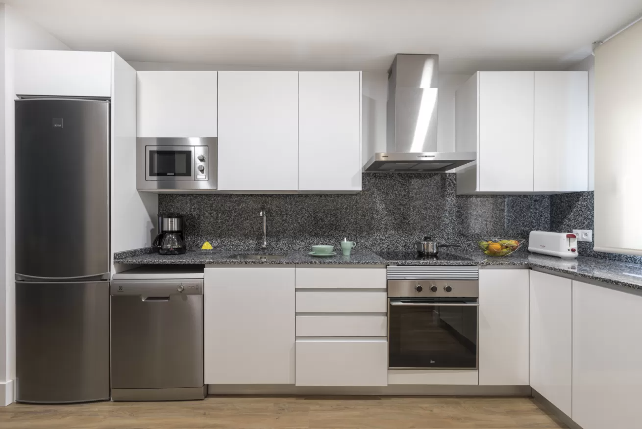 Cocina moderna blanca con electrodomésticos de acero inoxidable y salpicadero de mosaico oscuro.