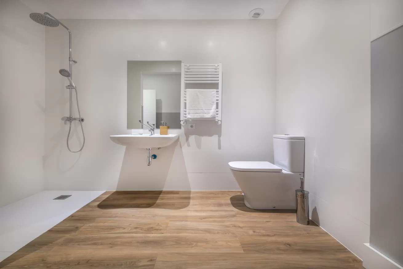 Baño moderno con ducha, lavabo mural, inodoro y suelo con aspecto de madera.