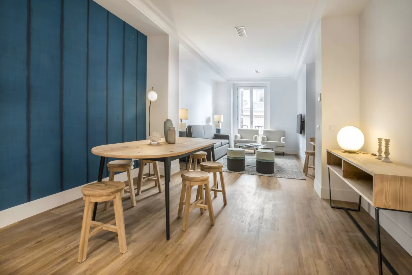 Salón-comedor luminoso y moderno con pared decorativa azul, mesa de madera y sofá.