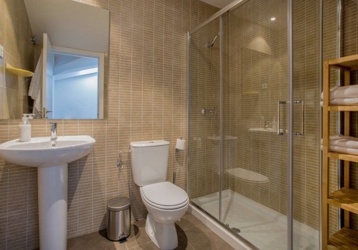 Baño con inodoro, lavabo con pedestal, ducha de cristal y paredes alicatadas en color beige.