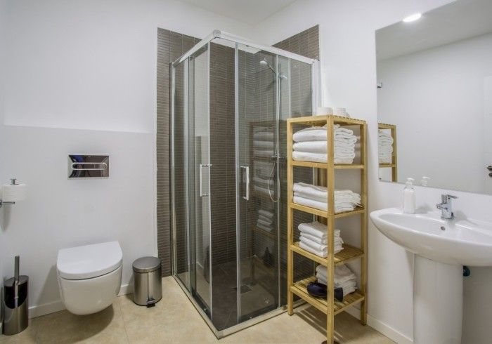 Baño pequeño con ducha, inodoro, lavabo y toallero en tonos neutros.