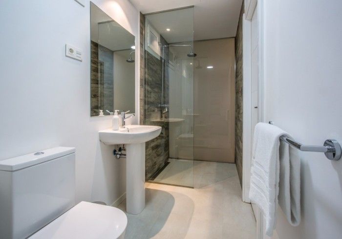 Baño moderno con inodoro, lavabo con pedestal, ducha de cristal y toallero.