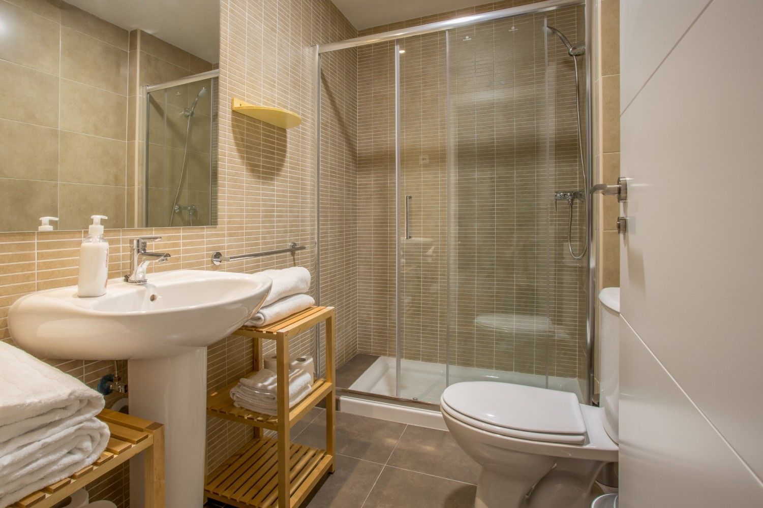 Baño compacto de color beige con lavabo, espejo, ducha e inodoro.