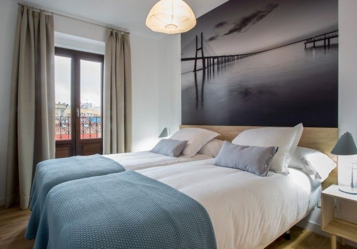 Habitación moderna con dos camas individuales, mantas azules, un gran cuadro en la pared y vistas al balcón.