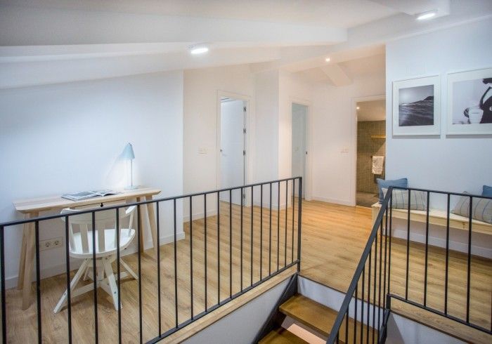 Distribuidor moderno tipo loft con barandilla negra, paredes blancas, suelo de madera y un pequeño escritorio.