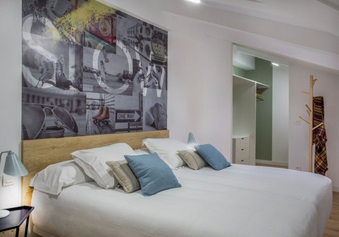 Dormitorio moderno con cama blanca, almohadas azules, cuadros en la pared y puerta de armario abierta.