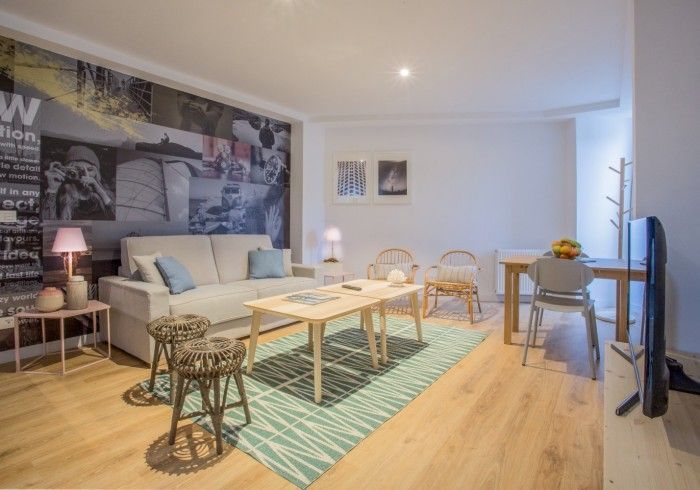 Sala de estar luminosa con sofá beige, mesas de centro de madera, alfombra color turquesa, zona de comedor y cuadros.