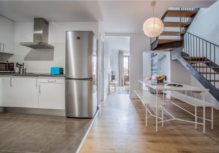 Cocina y comedor modernos de planta abierta con nevera de acero inoxidable, mesa blanca y escalera.