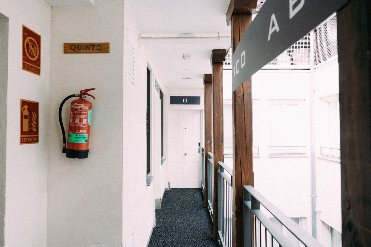 Pasillo blanco con un extintor rojo montado en la pared y puertas a lo largo del corredor.