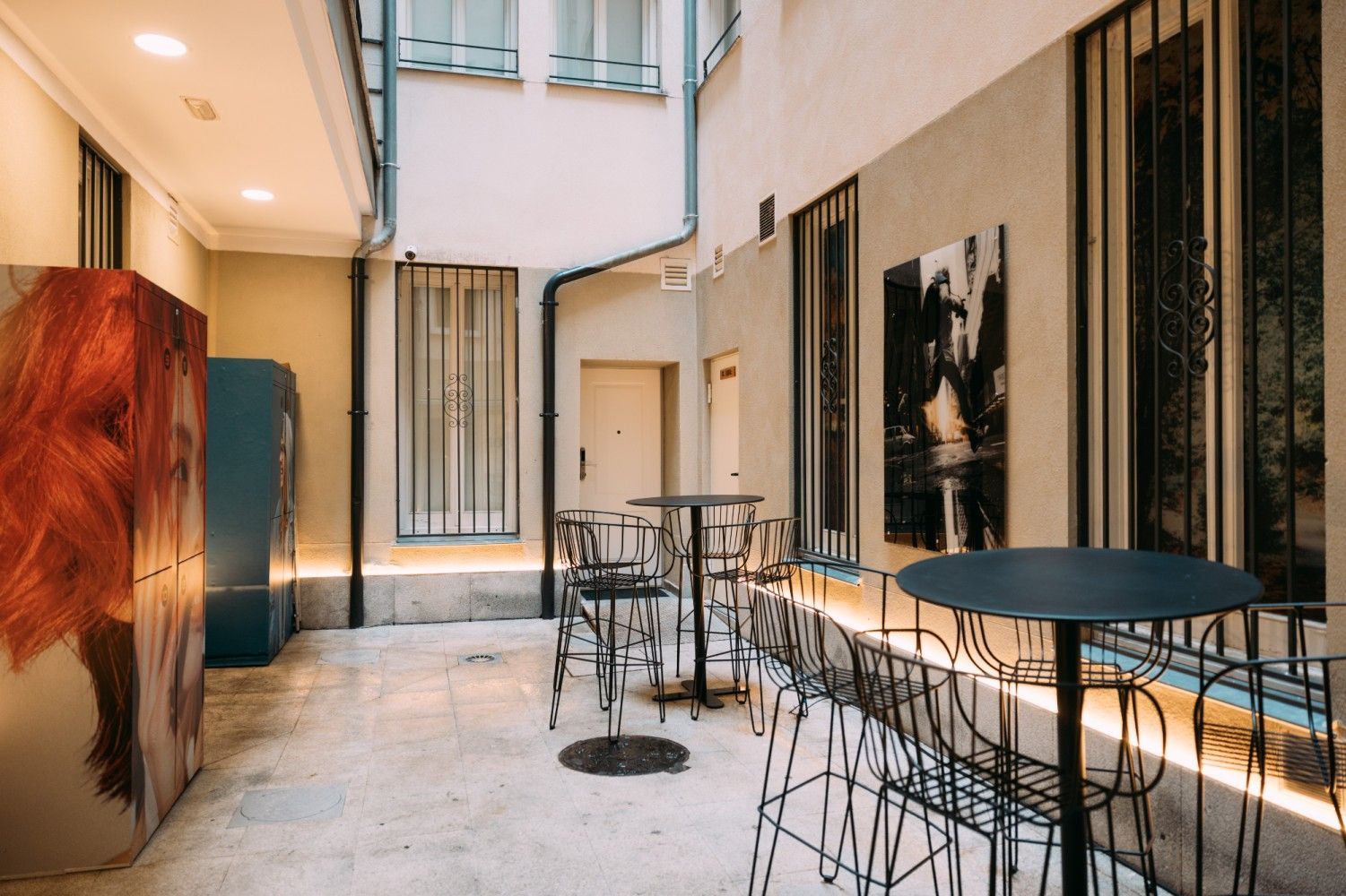 Cafetería moderna con patio, mesas y sillas de alambre, cálidos paneles de madera y grandes ventanales en un pasillo.