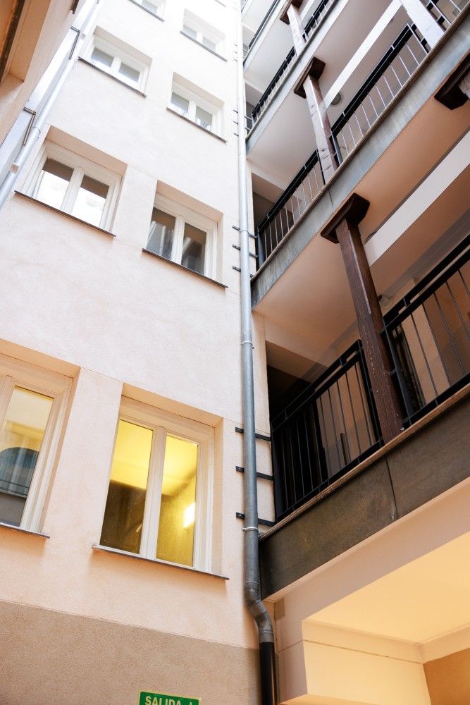 Patio alto entre edificios de apartamentos con paredes blancas, ventanas y balcones de metal oscuro.