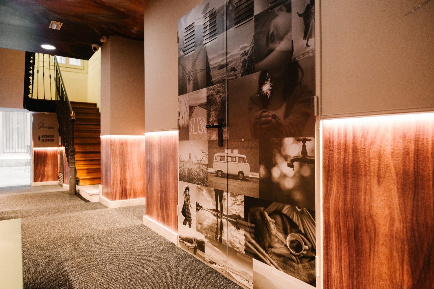 Pasillo con poca luz, paredes revestidas de madera, suelo enmoquetado y un gran mural fotográfico en tonos sepia.
