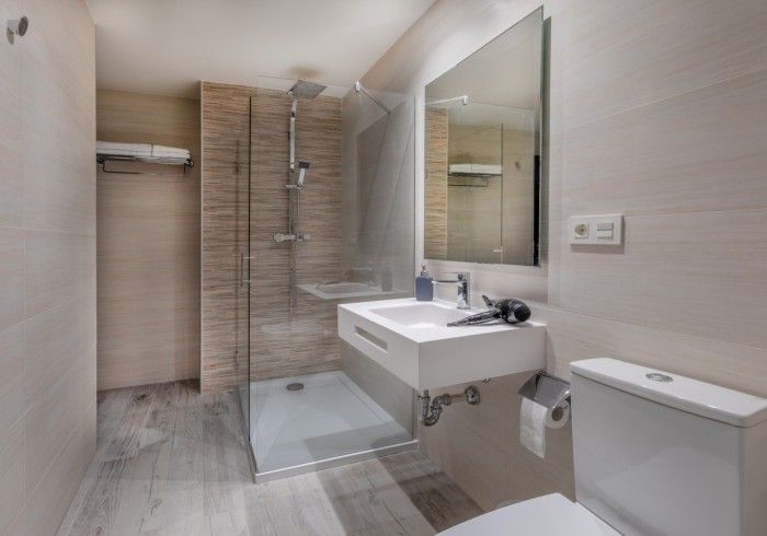 Baño moderno con ducha a ras de suelo, lavabo mural, espejo e inodoro en tonos neutros.