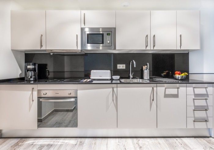Cocina moderna con gabinetes blancos, electrodomésticos de acero inoxidable y encimera con protector.