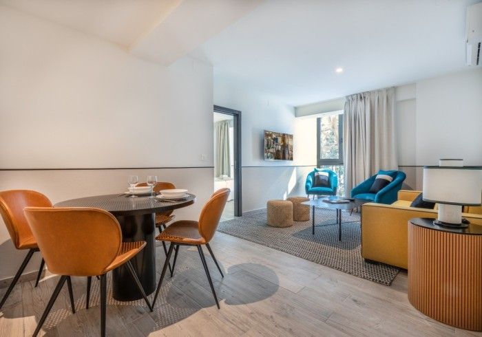 Apartamento moderno con sala de estar-comedor, sofás azules, sillas naranjas y grandes ventanales.