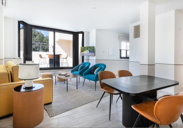 Sala de estar moderna y luminosa con puertas que dan al balcón, sillas azules, sofá color canela y mesa de comedor oscura.