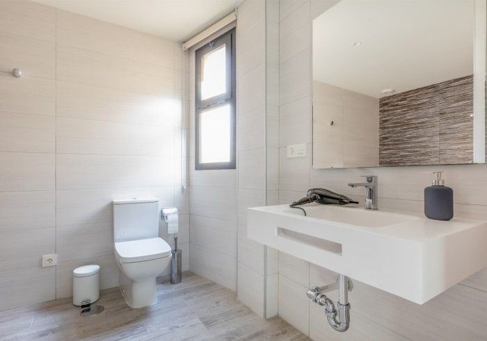 Baño moderno con inodoro, lavabo mural, espejo grande y zona de ducha alicatada.