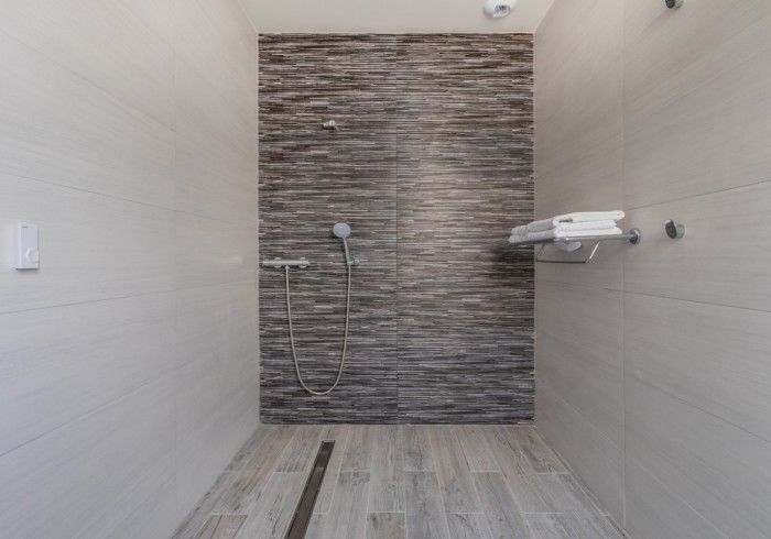Ducha moderna vacía con paredes alicatadas, desagüe a ras de suelo, cabezal de ducha de mano y estante montado en la pared.