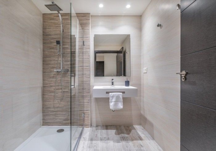 Baño moderno con ducha a ras de suelo, lavabo, espejo y paredes alicatadas en tonos neutros.