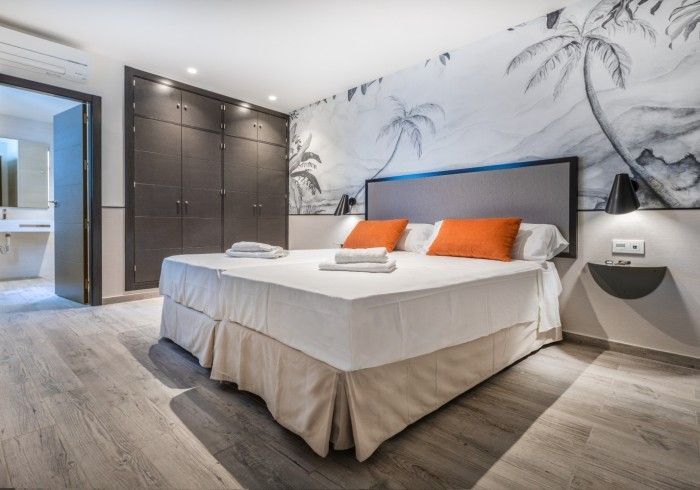 Dormitorio moderno con una cama grande, almohadas naranjas, armario empotrado y un mural de pared con motivos playeros.