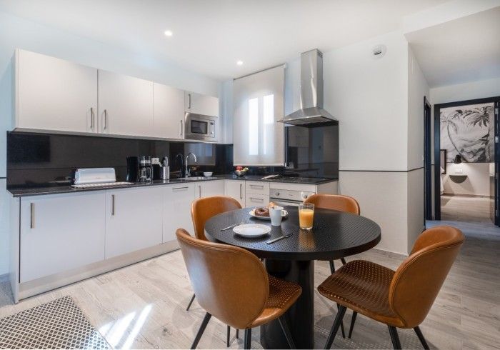 Cocina moderna con gabinetes blancos, salpicadero negro y una mesa de comedor redonda con cuatro sillas marrones.