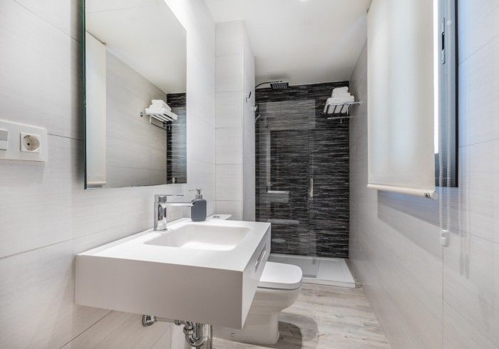 Baño moderno de color blanco con lavabo suspendido, espejo y ducha a ras de suelo.